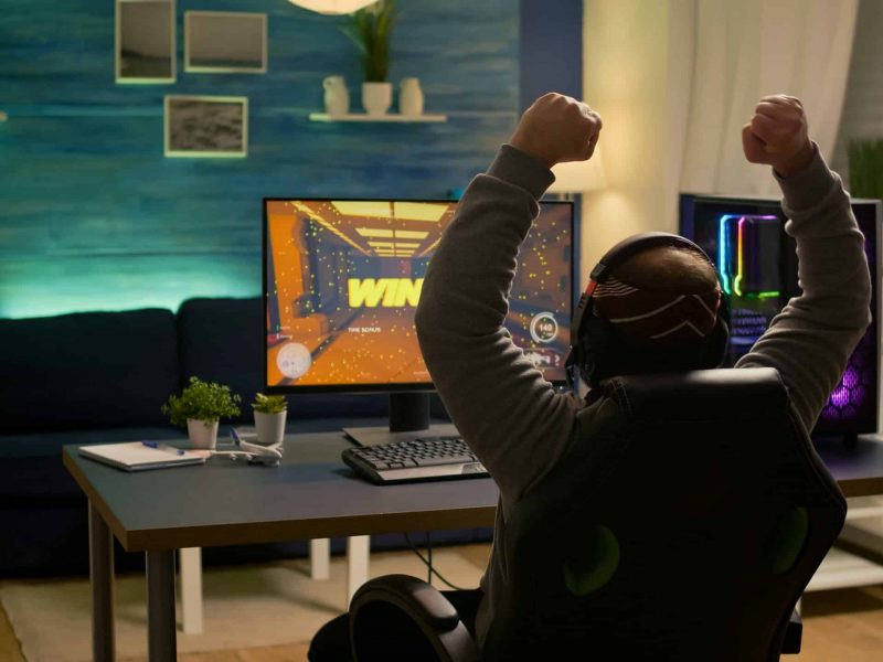 Videogamer player raising hands after winning first person shooter competition wearing hradphones. Professional pro gamer playing online video games with new graphics on powerful computer